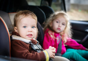 Twee jonge kinderen veilig vast in de auto, één in een kinderzitje en één met een autogordel op de achterbank.