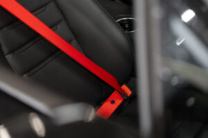 Rode autogordel over een geperforeerde zwarte lederen stoel van een Porsche.