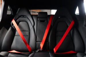 Achterbank van een Porsche met drie zwarte sportstoelen en felrode autogordels.
