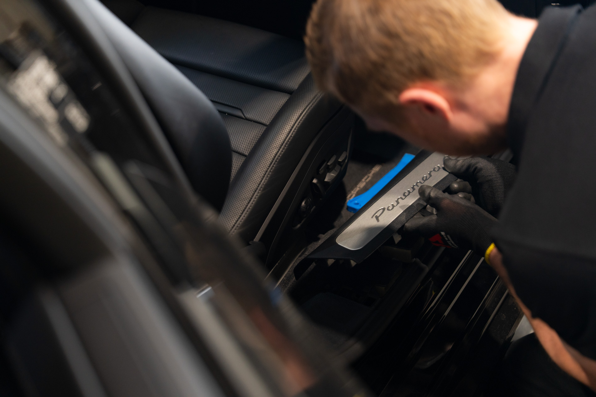 Medewerker van Autogordel.nl monteert een drempelplaat met Panamera-logo in een zwarte Porsche-interieur.