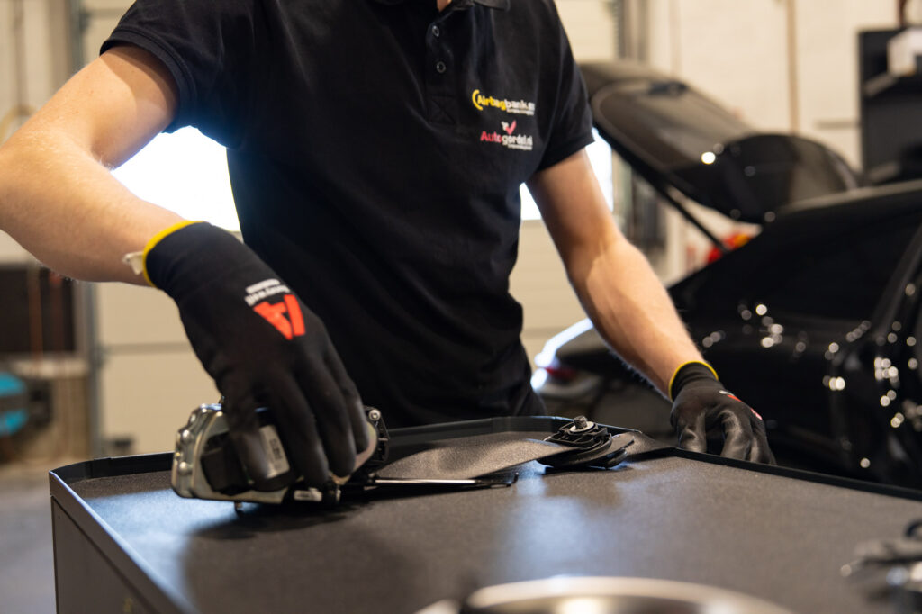 Monteur van Autogordel.nl met werkt aan een zwarte autogordel op een werkbank in een garage.