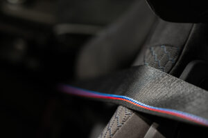Zwarte autogordel met BMW M-kleuren in een sportstoel met blauwe stiknaden.