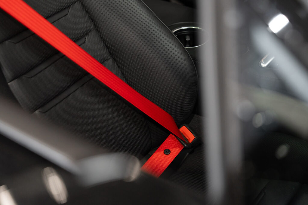 Close-up van een rode gepersonaliseerde autogordel in een zwarte sportstoel, perfect passend bij het interieur van de auto.