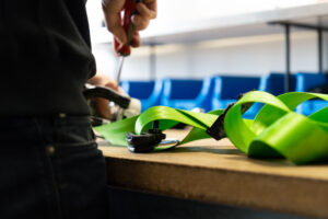 Medewerker van Autogordel.nl monteert een felgroene custom autogordel op een werkbank voor veilige installatie.