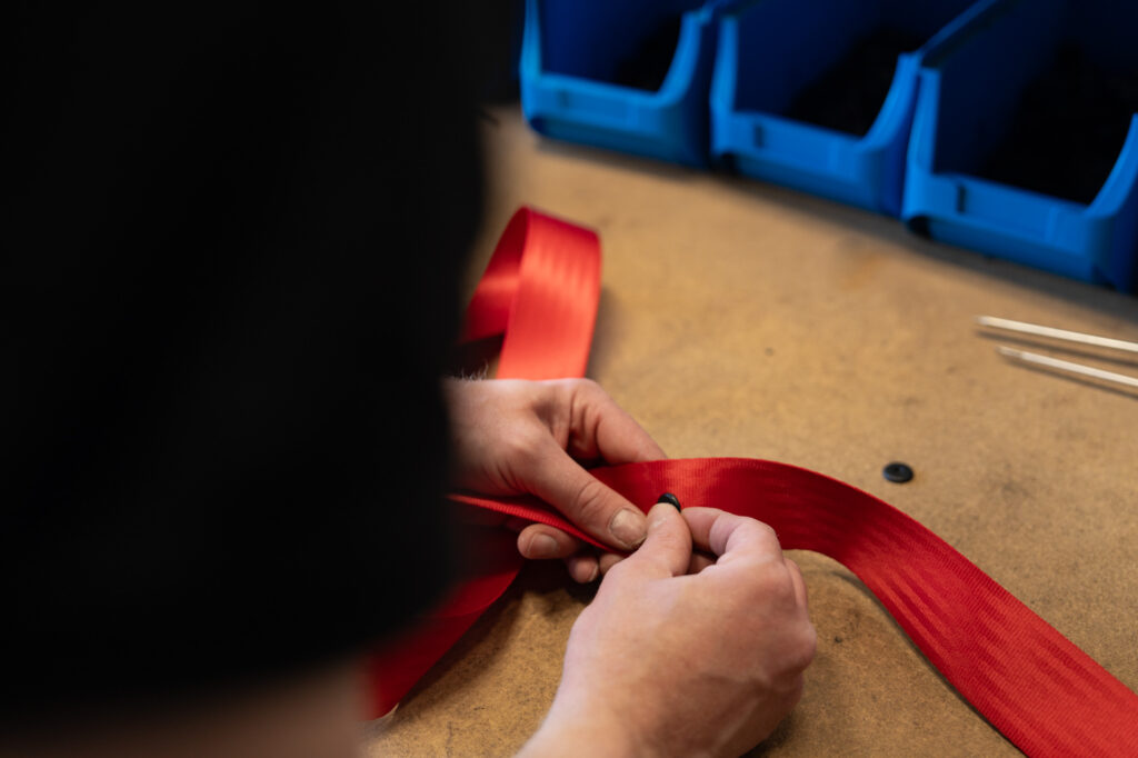 Monteur bevestigt onderdelen aan een rode autogordel tijdens het personaliseren in de werkplaats.