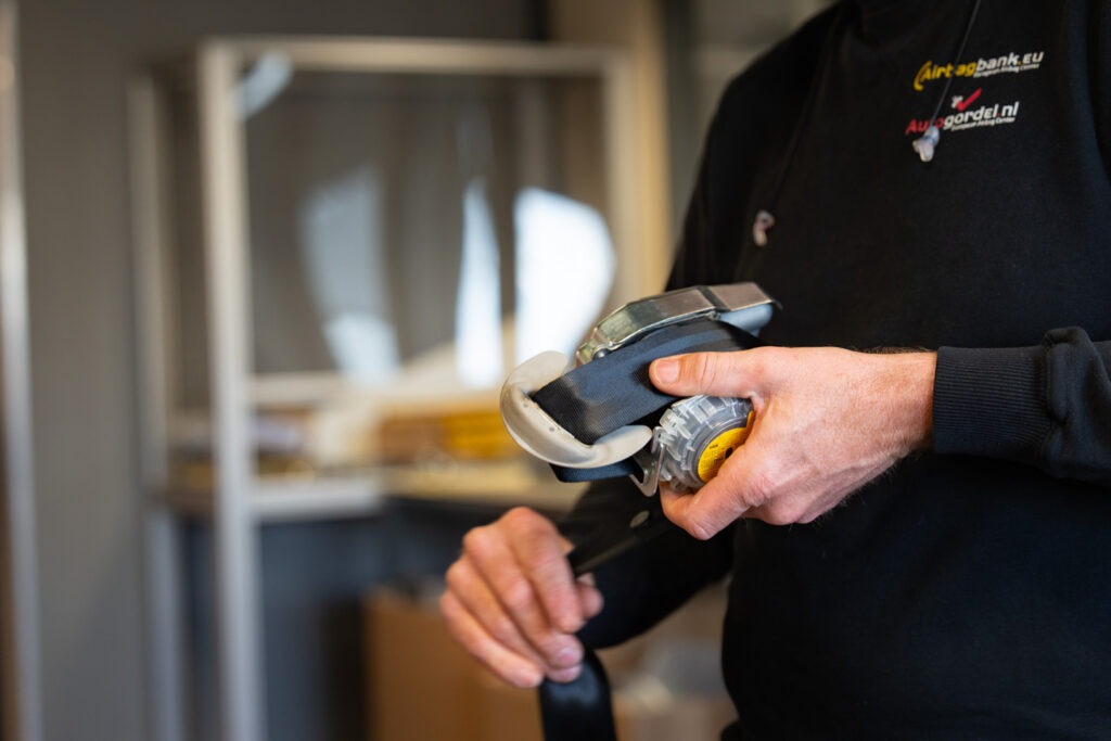 Specialist van Autogordel.nl controleert een zwarte autogordel met oprolmechanisme tijdens een technische inspectie.