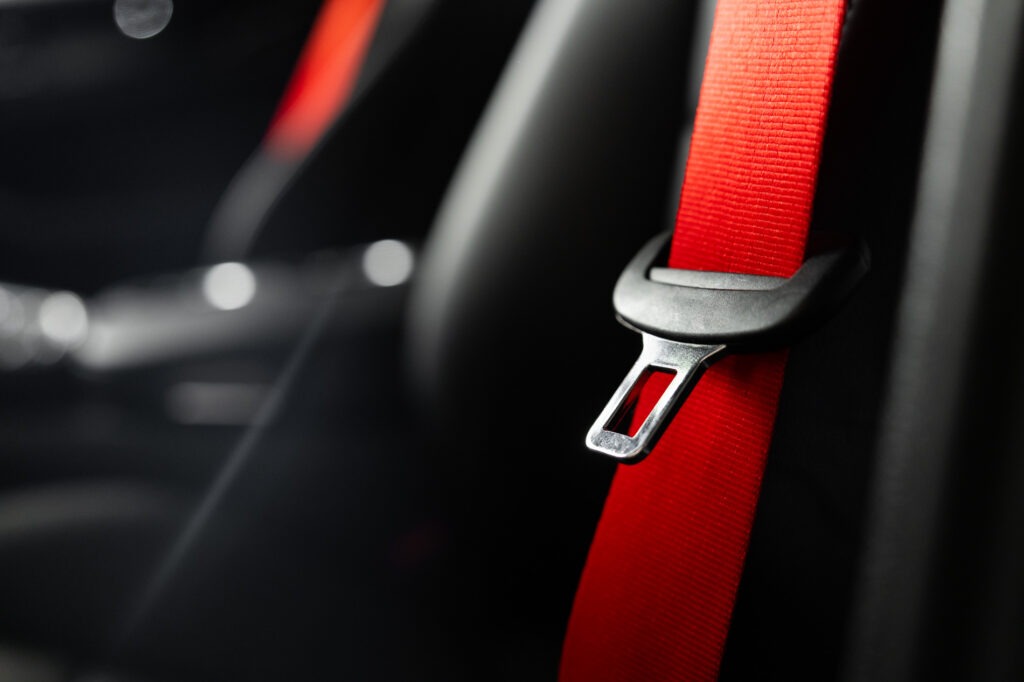 Close-up van een rode autogordel met metalen gordeltong in een zwart auto-interieur.