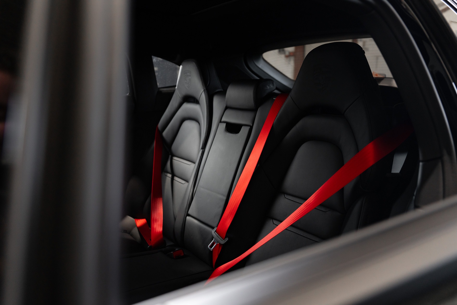 Rode gekleurde autogordels voor en achter in een zwart lederen auto-interieur, als voorbeeld van kleurcontrast in een donker interieur.